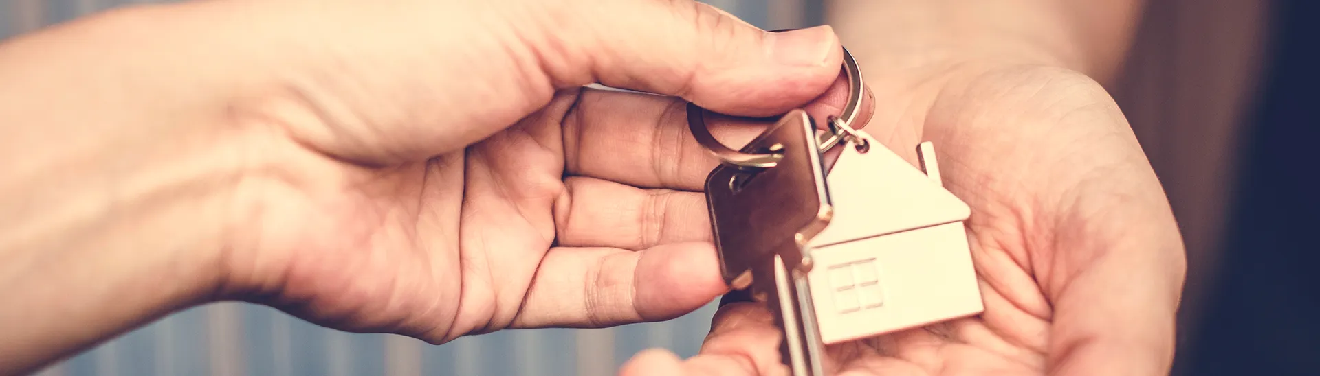 Holding keys between two hands with a house ornament attached to the keychain with the key.