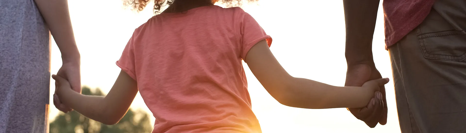 A young girl holding hands with her parents from the back with the focus on the little girl.