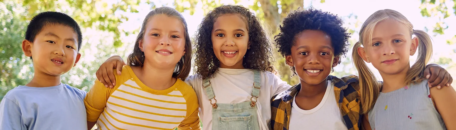 Grupo de niños de diferentes etnias sonriendo con las manos en los hombros de los demás.