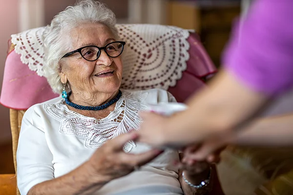 Woman-in-Chair-Receiving-Assistance An older woman receives assistance through the MFP program from a caregiver in her own home.