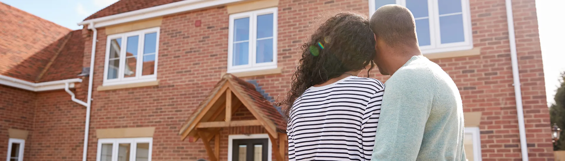 A couple hugging each other as they face their new home they're moving into.