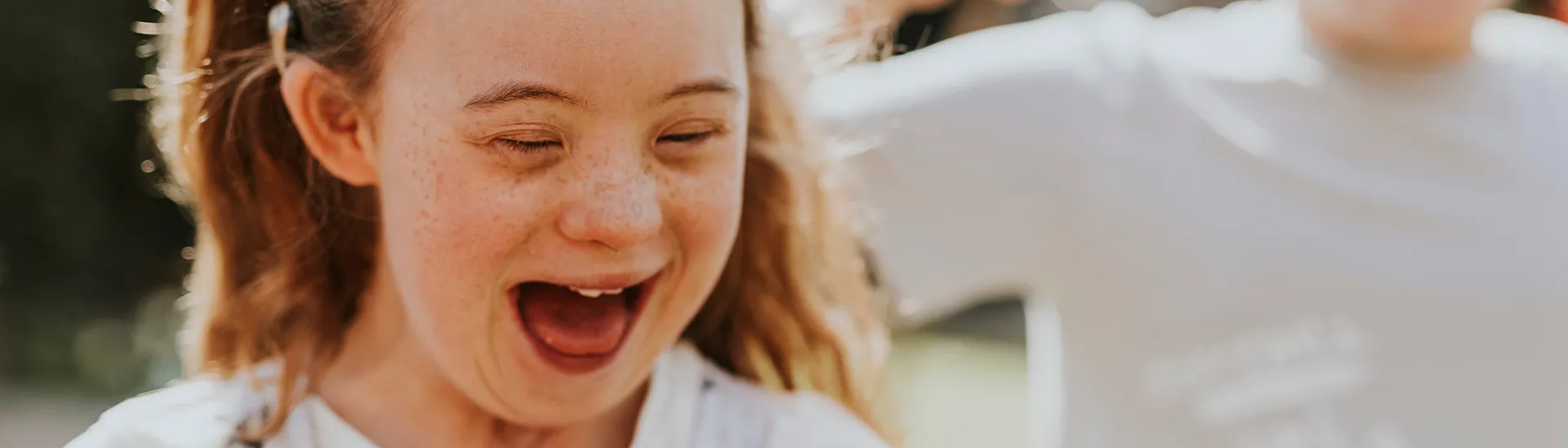 A young girl with down syndrome smiling and laughing while creating bubbles with another boy.