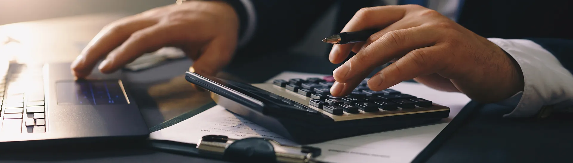 A man calculating financial information using a calculator and a laptop.