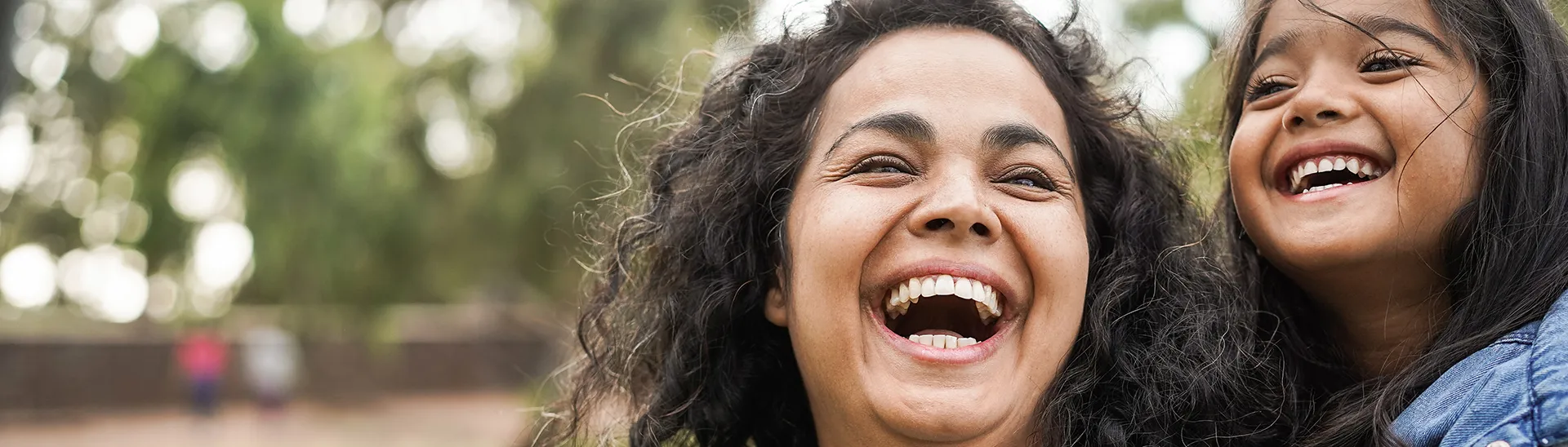 A mother with her daughter on her back are both laughing together.