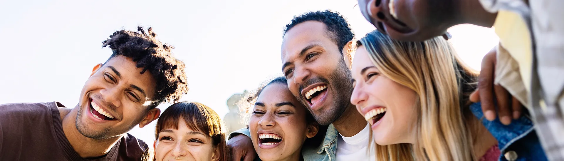 Un grupo de diferentes hombres y mujeres sonriendo y riendo con sus brazos alrededor de los hombros de los demás.