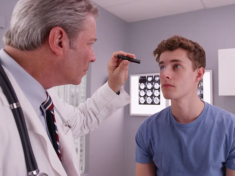 A doctor is giving his male patient an eye exam to check for any head trauma at his appointment.