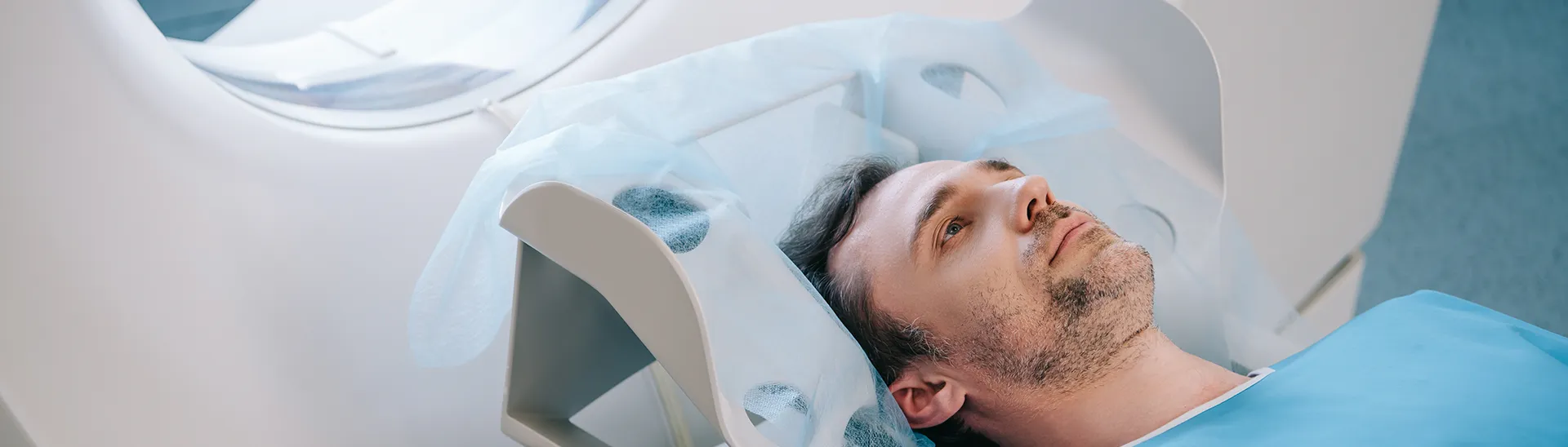 A man is laying in CT Scan machine about have his brain examined for any TBI-related trauma.