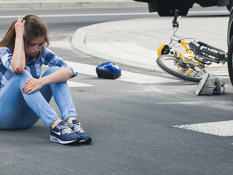 A woman sits, holding her head, after getting hit by a car while riding her bicycle.