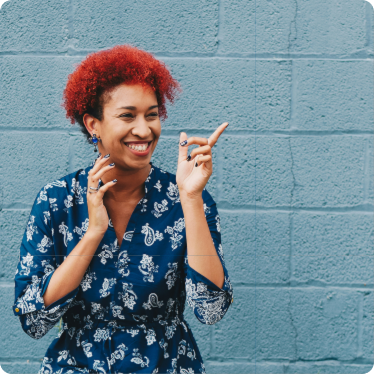 Girl with red hair and blue dress smiling with a blue brick wall behind her. 