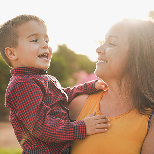 Una madre y su hijo sonríen juntos bajo la cálida luz del sol.