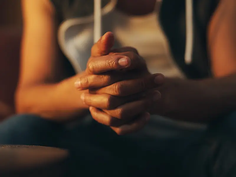 An African American man sitting with his hands folded asking for help.
